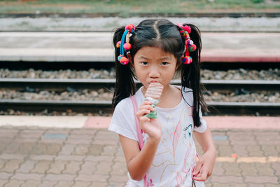 Portrait of girl eating ice cream while standing at railroad station platform