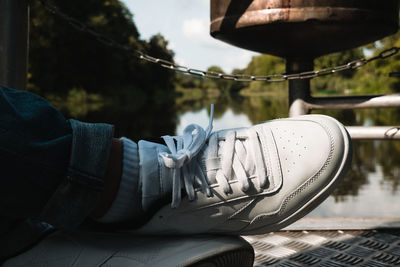 Low section of person wearing canvas shoe against lake