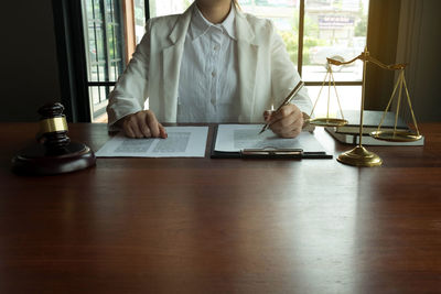 Midsection of woman holding pen over papers on table