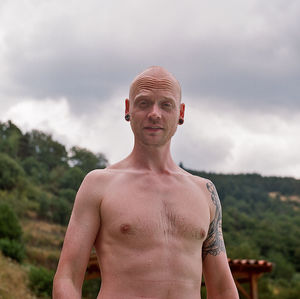 Portrait of shirtless man with tattoo standing on mountain against sky