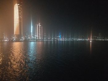 Illuminated city by river against sky at night