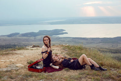 Two hippie woman are lying in a field on a mountain with an old gramophone on a vinyl record