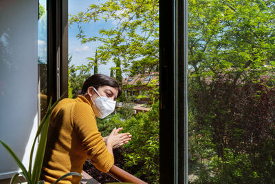 Woman wearing mask clapping while standing by railing against plants during quarantine