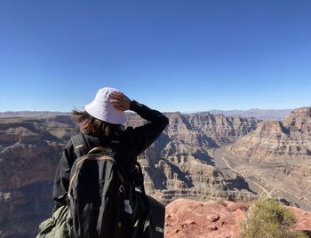 Rear view of man sitting on mountain against clear blue sky