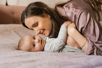 Satisfied mother kisses her sweet baby on the bed