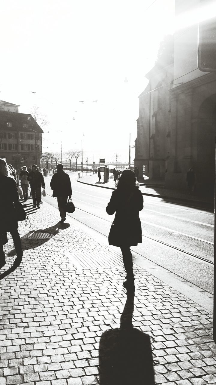 building exterior, lifestyles, walking, architecture, street, city, built structure, men, person, silhouette, city life, leisure activity, shadow, cobblestone, sidewalk, sunlight, clear sky, rear view