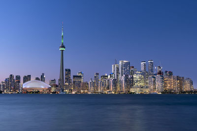 Illuminated buildings in city against clear blue sky