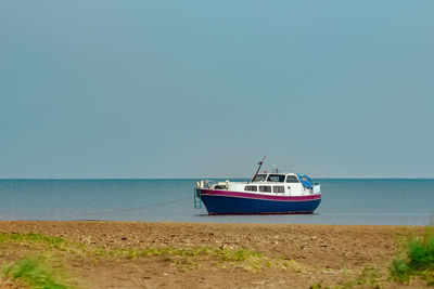 Boat moored on beach against clear sky