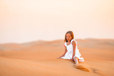 Full length of woman sitting on sand dune