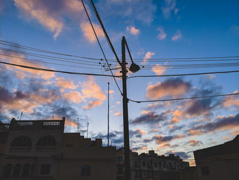 Low angle view of silhouette electricity pylon and building against sky