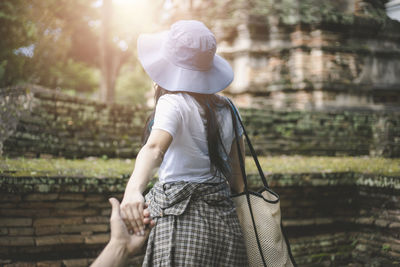 Rear view of woman holding man hand outdoors