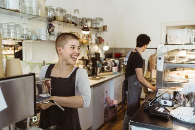 Young happy female owner looking away while preparing coffee in cafe