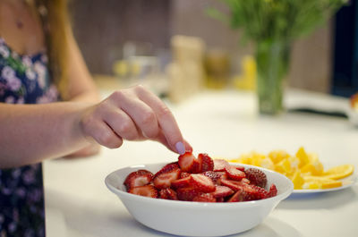 Midsection of woman touching chopped strawberries