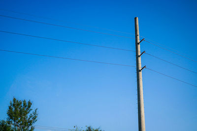 Low angle view of electricity pylon against clear blue sky