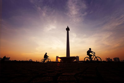 Silhouette people riding bicycle against sky during sunset