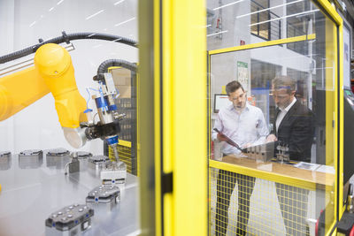 Two businessman observing industrial robots in factory