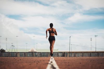 Rear view of female athlete running on track field against sky