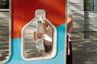 Woman pours drinking water into water bottle in city at refill water station. 