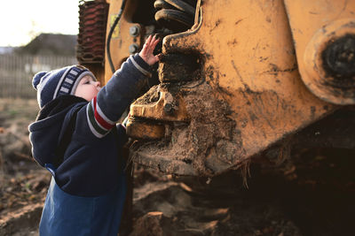 A boy in the village on the background of a tractor walks on the sand . 