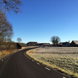 Empty road amidst field against clear blue sky