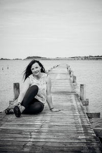 Portrait of young woman sitting on jetty over lake