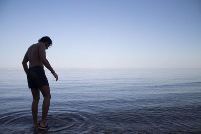 Full length of shirtless man standing in sea against clear sky