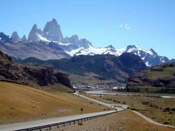 Empty road leading towards mountains against clear sky