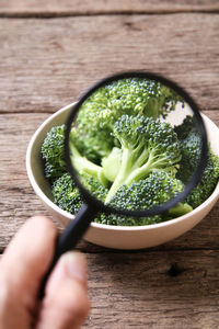 Cropped hand holding magnifying glass over broccoli