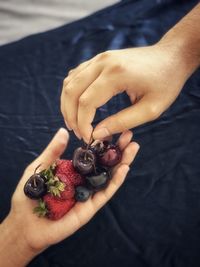 High angle view of female hand holding fruits and male hand picking up cherry.