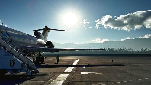 Airplane at airport runway against sky on sunny day