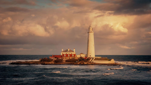 Lighthouse by sea against sky during sunset