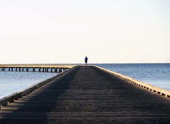 Man standing on pier over sea against clear sky