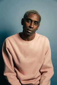 Adult african american male model in trendy pink sweatshirt looking at camera against blue background