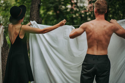 Rear view of shirtless man and woman standing against plants