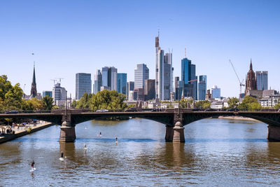 Bridge over river by buildings against clear sky