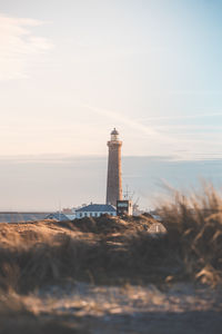 Lighthouse by sea against sky during sunset