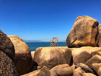 Rocks by sea against clear blue sky