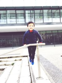 Full length portrait of smiling boy balancing on railing against building