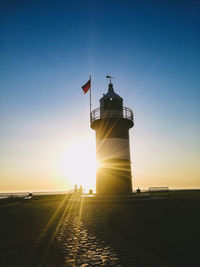 Lighthouse by sea against clear sky during sunset