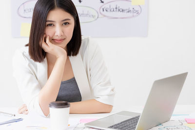 Portrait of young woman using phone while sitting on table