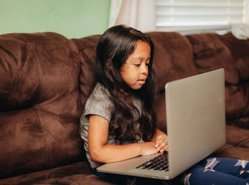 Mixed race young girl at home on the sofa using a laptop computer for learning
