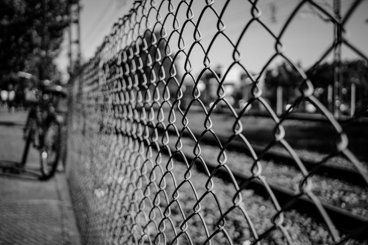 fence, chainlink fence, black and white, monochrome, black, security, protection, monochrome photography, focus on foreground, day, nature, no people, sports, metal, outdoors, white, architecture, chain-link fencing, selective focus, sky, line, close-up, wire fencing, city, tree, built structure