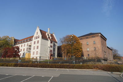 Road by buildings against clear blue sky