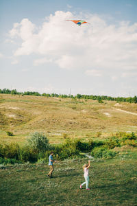 Couple flying kite on field against sky