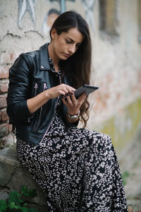 Bussineswoman with leather jacket and dress looking at her phone.