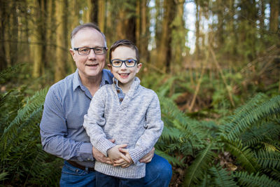 Grandfather holds his grandson in the forest.