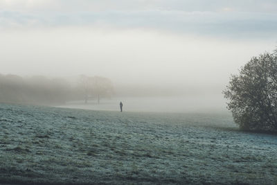 Scenic view of man on frosty field against sky during early morning in fog 