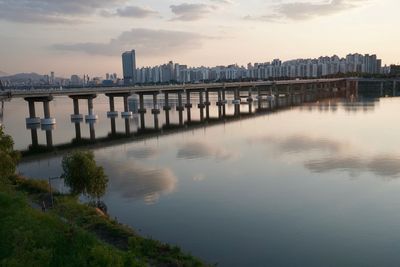 Scenic view of river by buildings against sky during sunset