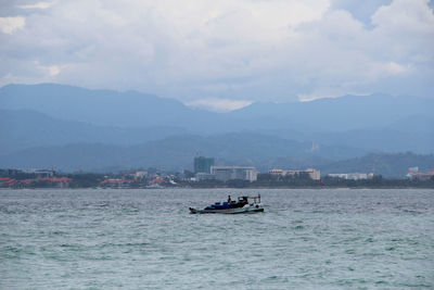 Boat sailing on sea by mountains against sky