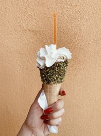 Close-up of hand holding ice cream against wall